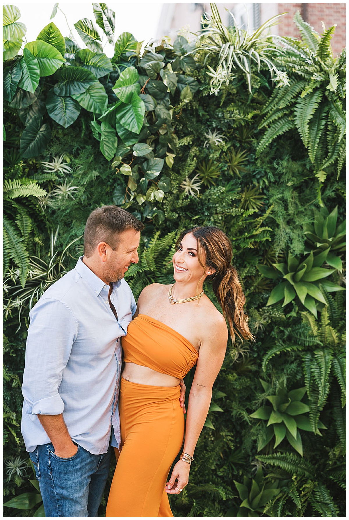 A couple posing in front of a tropical grass wall.