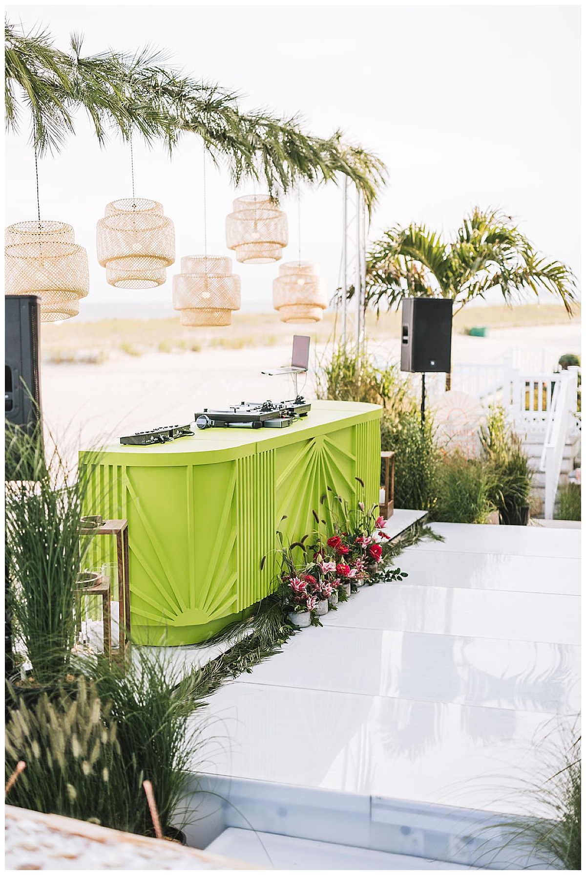 A lime green DJ booth set up on the beach under hanging bamboo pendant lights.