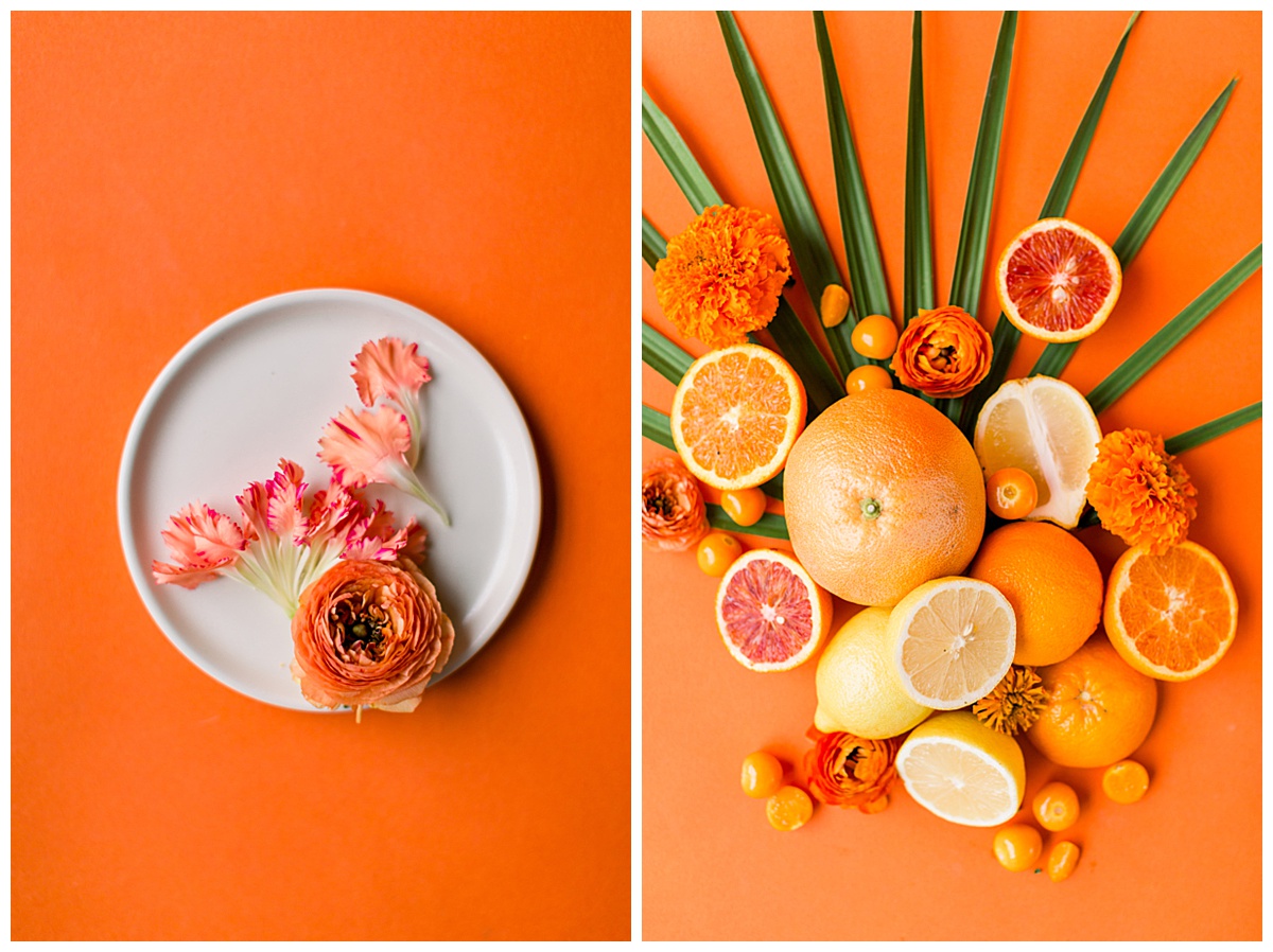 A white plate topped with florals in sunset-inspired hues and vibrant, tropical fruit artfully arranged over a green palm leaf.