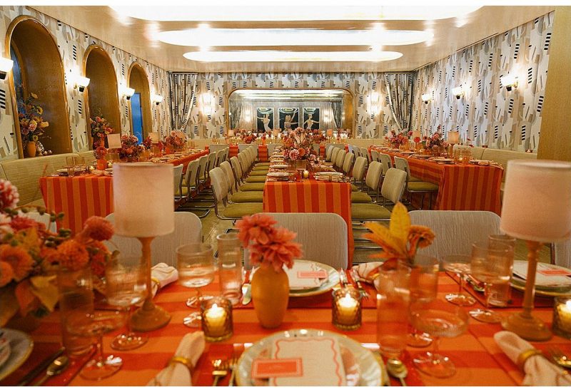 Vibrant event setup with orange-striped table linens and lush floral centerpieces, celebrating Verona Sunset for Brides x Minted event, styled by Something Vintage Rentals.