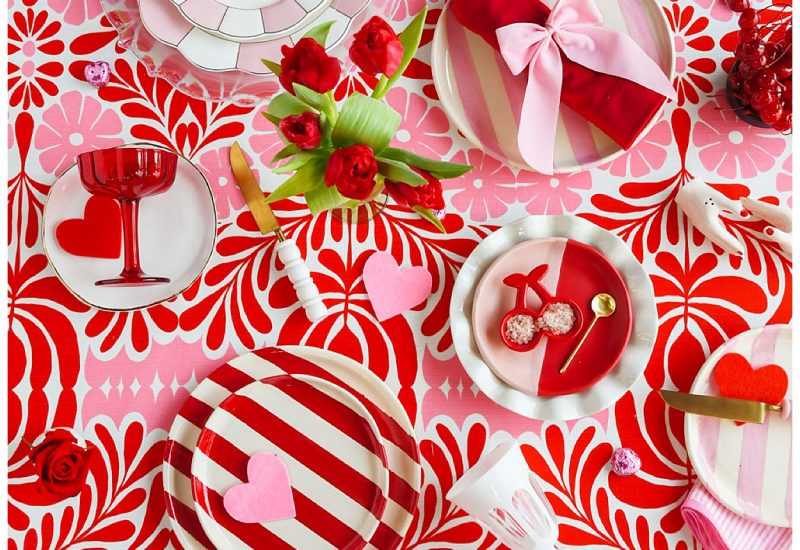 A beautifully detailed Valentine's Day tablescape with layered plates, gold and pink flatware, and charming cherry-shaped salt dishes. Red and pink roses overflow from the centerpiece, creating a lush, romantic aesthetic. Rentals by Something Vintage Rentals, the U.S. East Coast’s best event rental and wedding decor company.