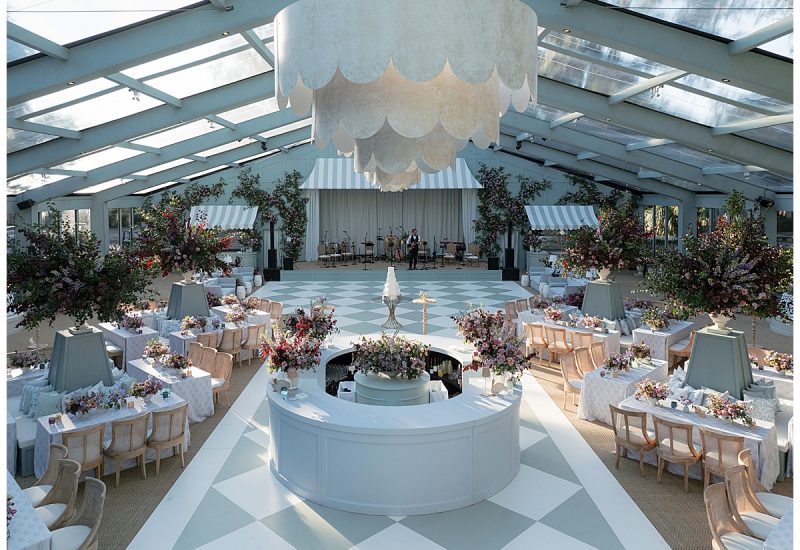 Rows of banquet tables with pastel linens, lush floral arrangements, and wood chairs under a clear tent. Rentals by Something Vintage Rentals, the U.S. East Coast’s best event rental and wedding decor company.