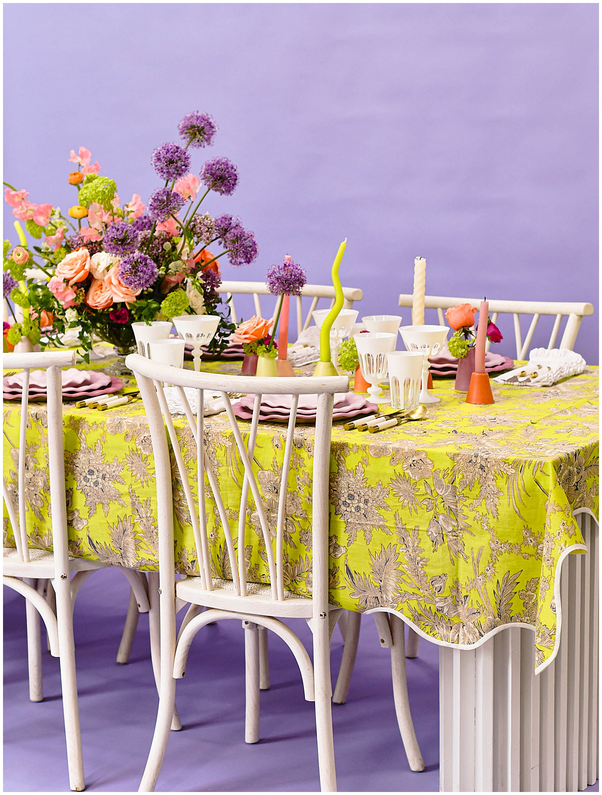 Vibrant spring tablescape with lilac backdrop, green floral tablecloth, and pastel florals styled with white vintage chairs, part of the OG linen collection from Something Vintage Rentals, the U.S. East Coast’s best event rental and wedding decor company.