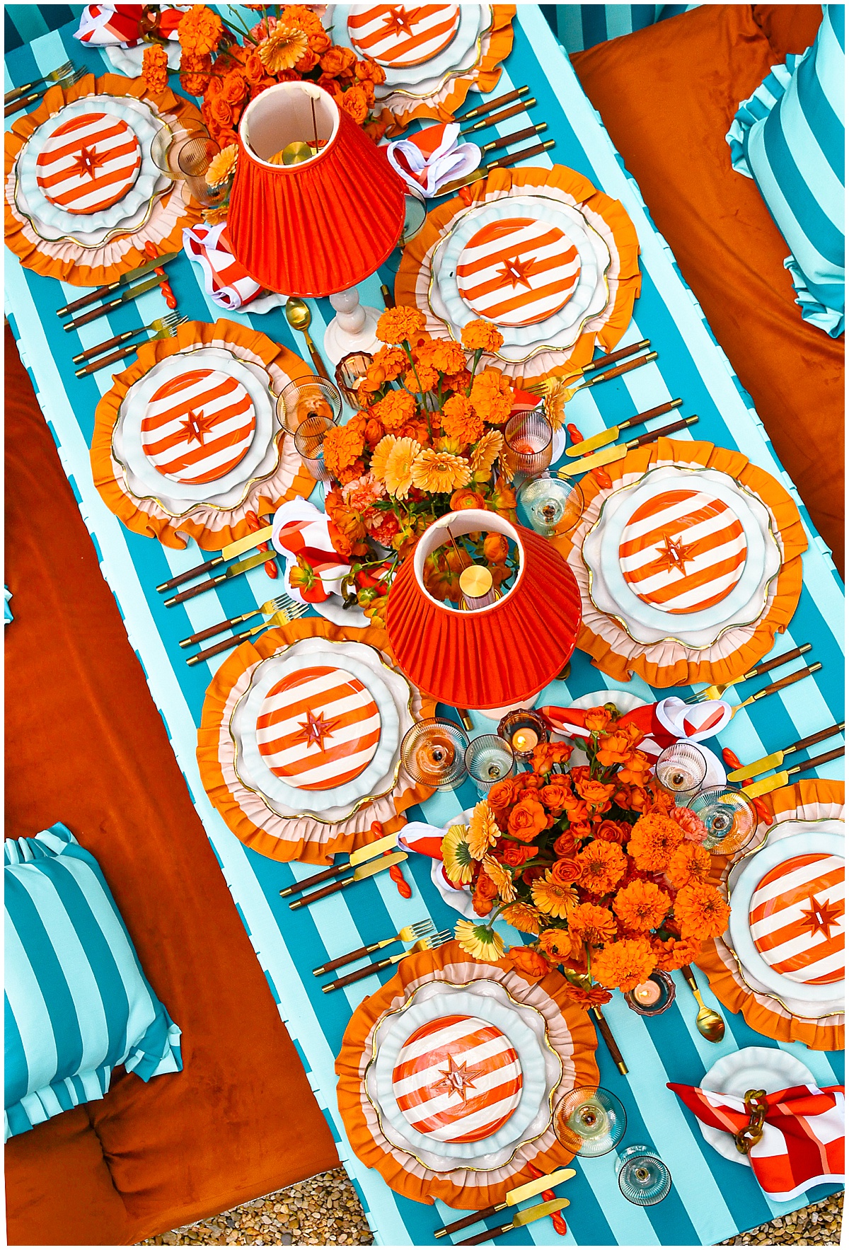 Overhead view of teal striped tablescape with orange ruffled chargers, striped salad plates, red pleated lampshades, and orange florals for 2026 wedding trends by Something Vintage Rentals