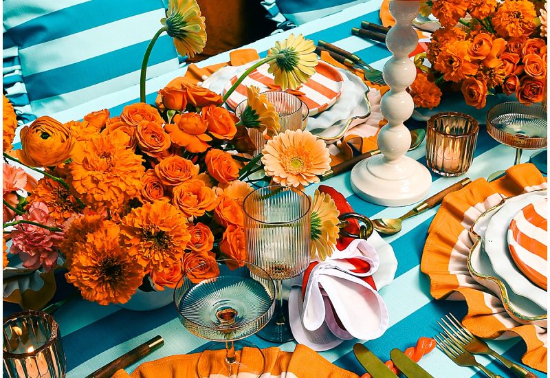 Teal striped tablescape with orange ruffled chargers, striped salad plates, red pleated lampshades, and orange florals for 2026 wedding trends by Something Vintage Rentals