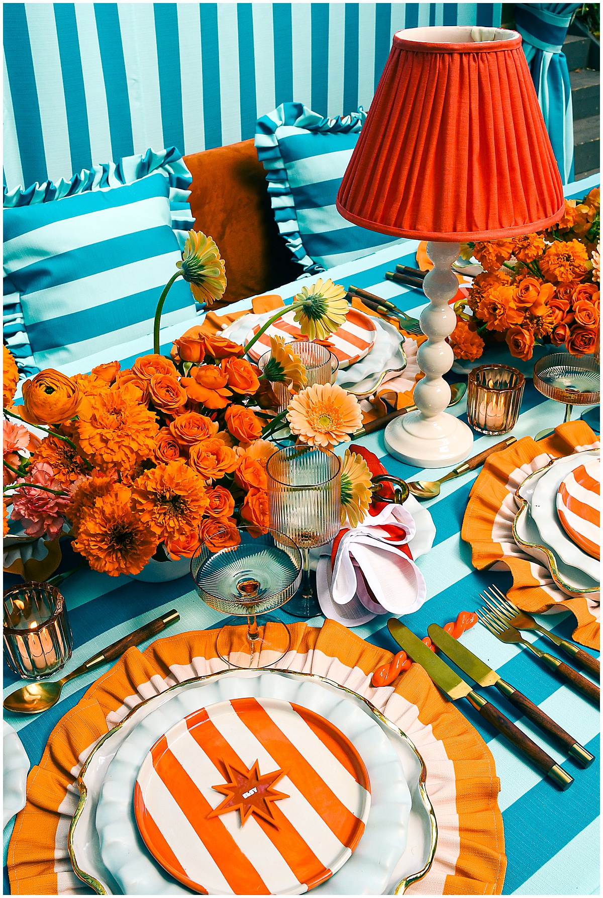 Teal striped tablescape with orange ruffled chargers, striped salad plates, red pleated lampshades, and orange florals for 2026 wedding trends by Something Vintage Rentals
